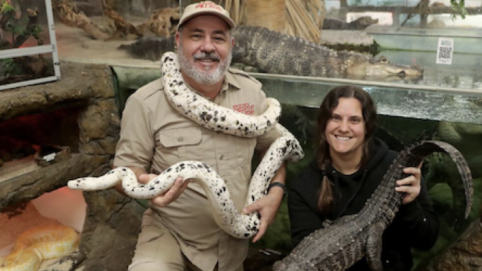 Reptile Royalty TV show screenshot 1: Jay brewer stands with a white snake around his neck while his daughter Laura stands to his right. 