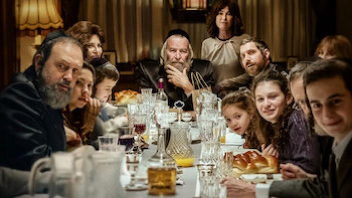 Still from Rough Diamonds: An Orthodox Jewish family of adults and children sits at a table filled with food and drinks.
