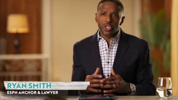 Scam Goddess TV show screenshot 2: ESPN anchor Ryan Smith wears a suit jacket and talks to the camera while sitting at a desk