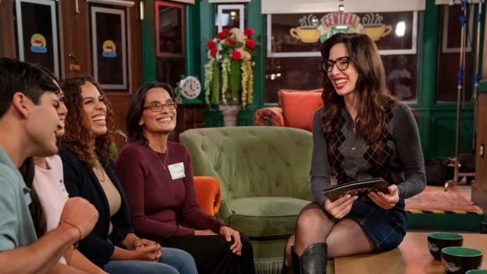 Fast Friends: Whitney Cummings sits on the coffee table across from four contestants sitting on a couch in the Central Perk set.
