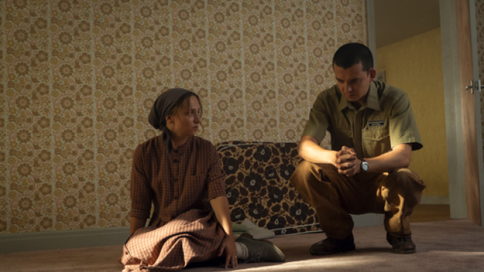 Unchosen TV show screenshot 3: A woman and a man in uniform sit on a carpeted floor in a dimly lit room.