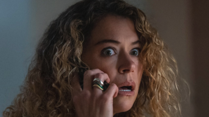 Woman with curly hair looks shocked while on a phone call.