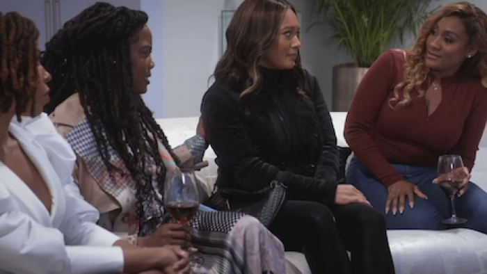 Sistas screenshot 3: Women sit on white sofa drinking wine. 