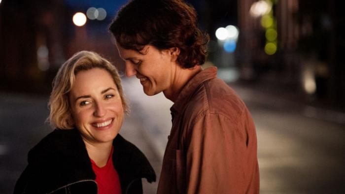 Slip: Elijah and Mae are shown in medium close-up; both are laughing. They're on a city street at night. 