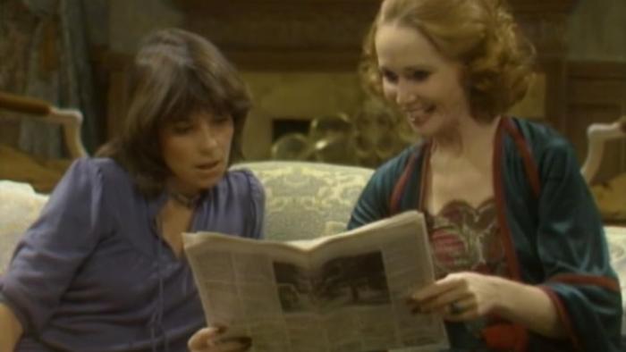 Soap: Eunice and Jessica sit together on an elegant living room couch, looking at a story in a newspaper