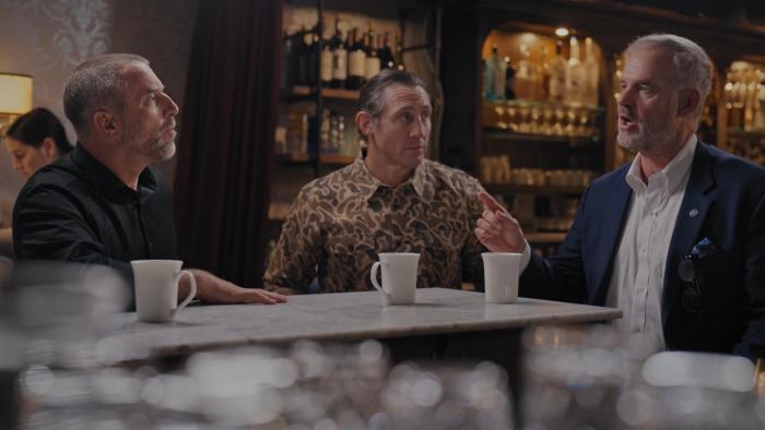 From Left to Right: Jeff Tiegs, Tim Kennedy, and David Johnson sit in a bar. There are white coffee mugs on a counter in front of them.