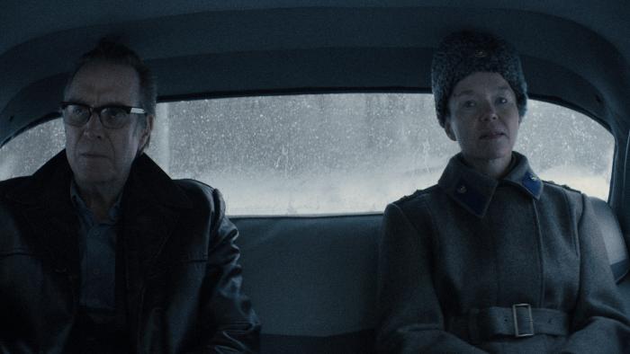 Rhys Ifans and Anna Maxwell Martin sit in the backseat. Ifans wears a leather coat with fur. Martin wears a coat and a fur hat.