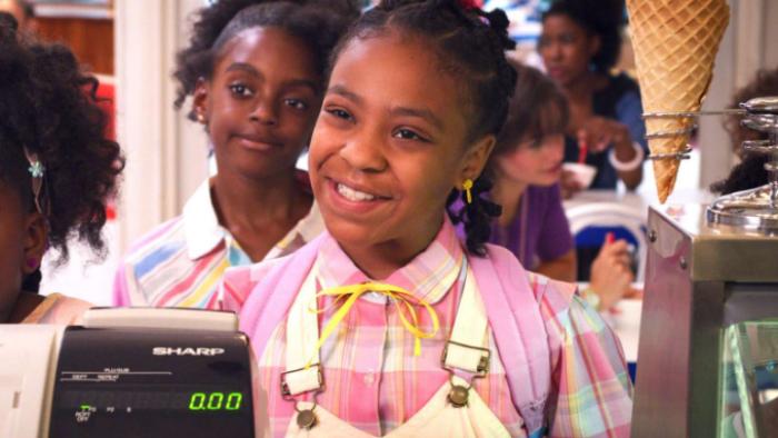 Stranger Things 3 TV show screenshot 3: Erica smiles in front of a cash register, dressed in a pink 1980s dress