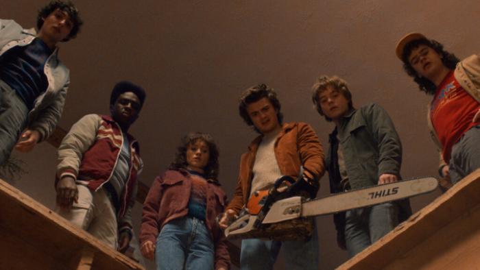 Stranger Things Season 5 TV show screenshot 2: Mike, Lucas, Nancy, Steve, Robin, and Dustin look down from a hole in a ceiling; Steve holds a chainsaw
