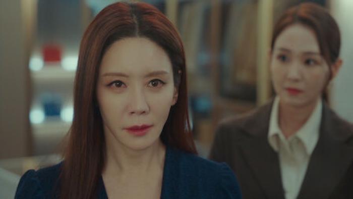Jeong-eun Kim as Hwang Geum-ju, stands in front of a woman.