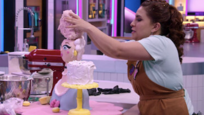 Sugar Rush: The Baking Point TV show screenshot 1: A contestant in a brown apron and white shirt adds fondant to a cake layer. 