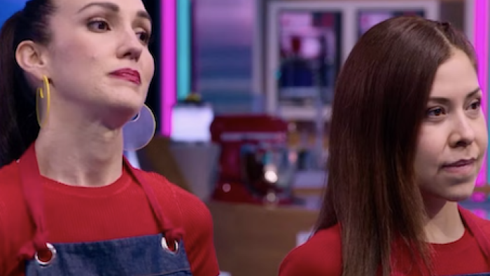 Sugar Rush: The Baking Point TV show screenshot 3: Two female contestans in red shirts and denim aprons look pained as judges talk to them.