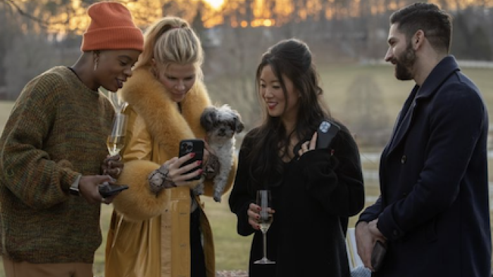 Swiping America TV show screenshot 2: Ashley, Reagan, Keson, and  Krishnanand look at their phones together in outside in the cold in Ashville.