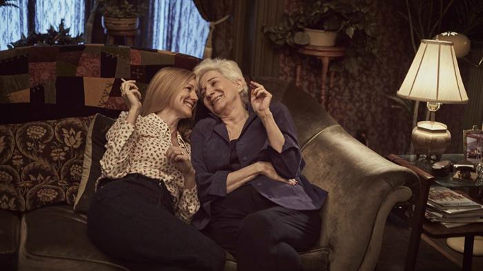 Tales of the City TV: Mary Ann and Anna snuggle close together on a Victorian couch, smiling while holding cigarettes