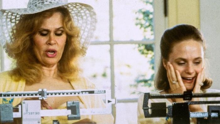 Tales of the City TV Show: Two women stand on side-by-side medical scales; one looks happy with her scale's reading, the other looks shocked. 