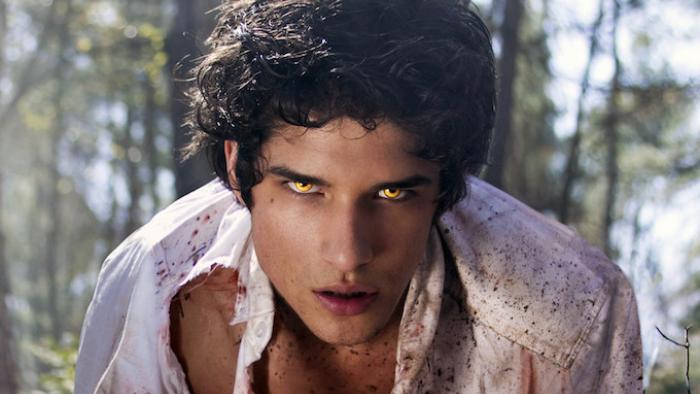 Young adult man with thick dark hair hunches over with glowing yellow eyes and a torn shirt