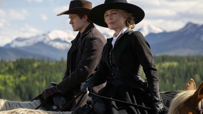 The Abandons TV show screenshot 2: Lucas Till and Gillian Anderson ride horses. They wear dark hats and dark overcoats. Mountains in the background.