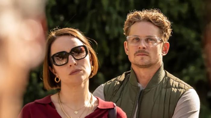 The Audacity screenshot 3: Sarah Goldberg wears a red blouse and dark shades. Billy Magnussen wears a grey shirt, green vest, and clear glasses.