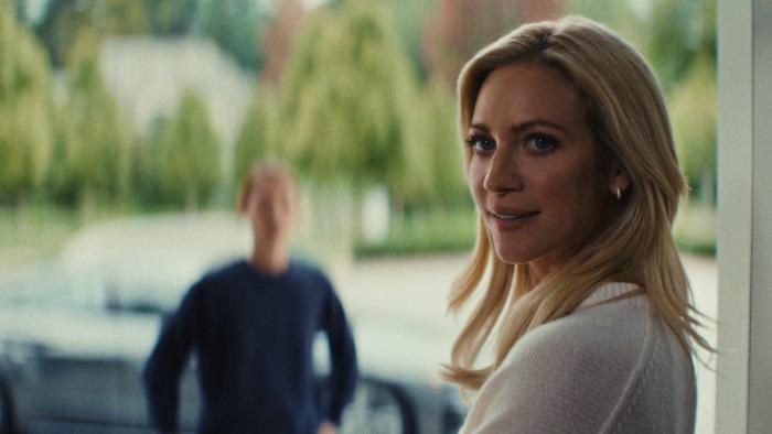 Brittany Snow looks over her shoulder while standing in a doorway. She wears a white sweater.