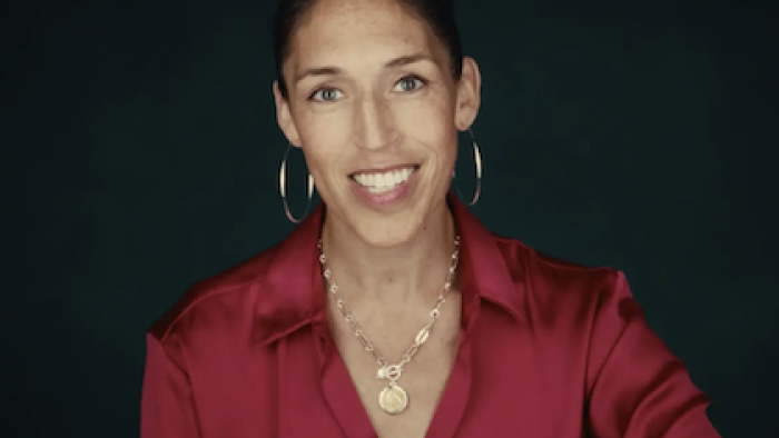 The Dynasty: UConn Huskies TV show screenshot 3: Smiling Rebecca Lobo in a red blouse, wearing hoop earrings and a necklace.