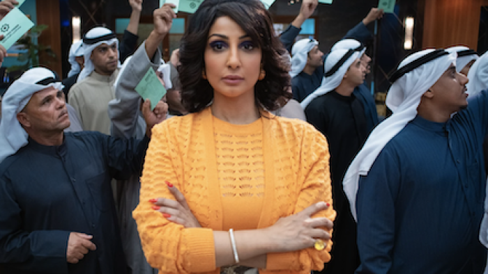 The Exchange TV show: Munira stands in front of Kuwaiti traders on the floor staring at camera with arms crossed. 