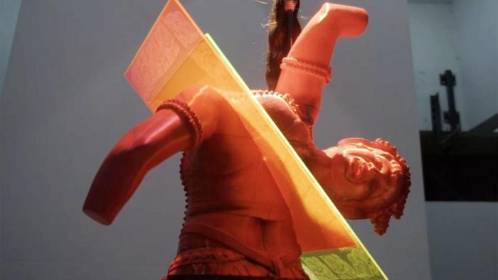 The Exhibit TV show screenshot: A red sculpture depicts the Statue of Liberty cut in half by a colorful red and yellow sheet of glass.