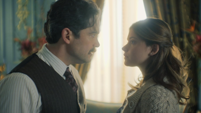 The House of the Spirits screenshot 3: Esteban and adult Clara face each other next to a curtained window.
