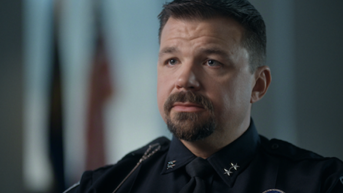 The Idaho Murders: College Nightmare screenshot 1: Police Chief Anthony Dahlinge in uniform, looking thoughtful, with flags blurred in the background.