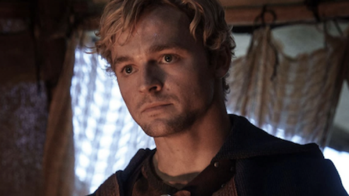 The Pendragon Cycle: Rise of the Merlin TV show screenshot 1: Taliesin with blonde hair in medieval attire looks serious indoors.