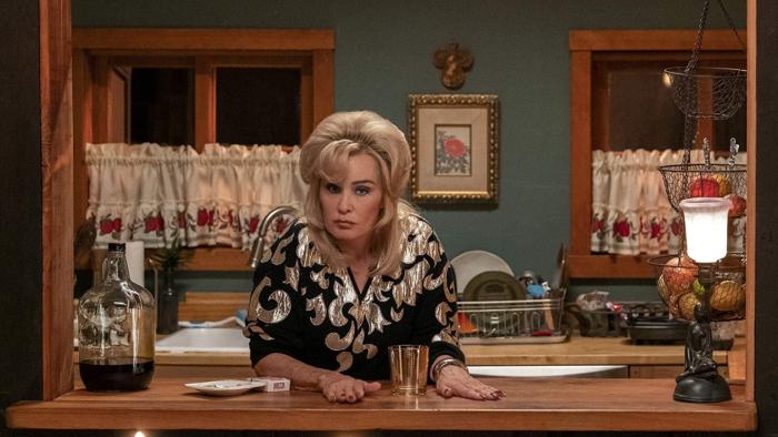 The Politician TV Series: Dusty looks out a window; a glass is in front of her, she's in a glitzy sweater, and looks regretful. 