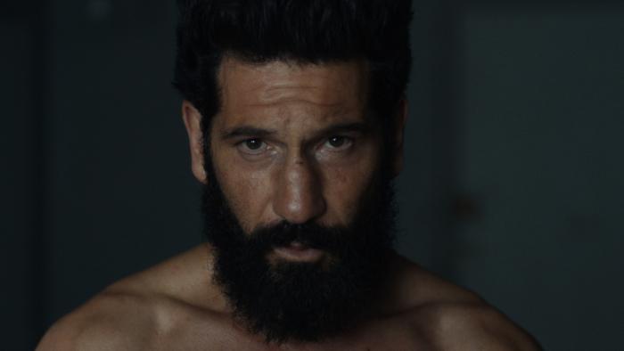 The Punisher: One Last Kill TV show screenshot 1: Jon Bernthal, shirtless, sits in a dark room by himself.
