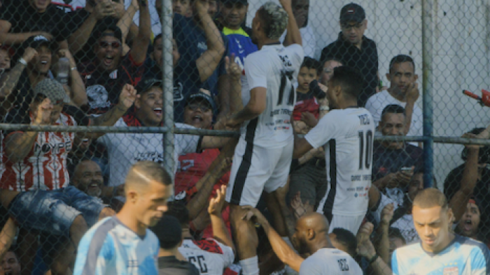 The Root of the Game TV show screenshot 2: Soccer players celebrating with cheering fans behind a fence.