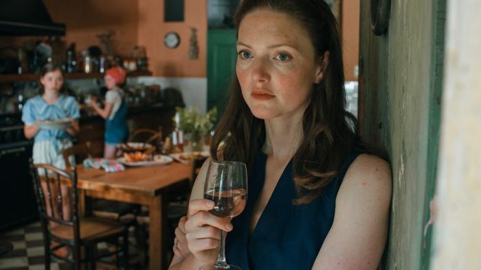 The Stolen Girl TV show screenshot 3: Holliday Grainger leans against a door frame while holding a glass of white wine.