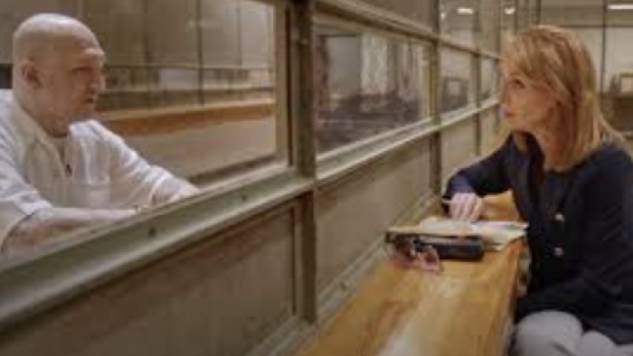 The Takedown: American Aryans TV show screenshot 2: Brown haired reporter talks through prison glass to former bald ABT member in white. 