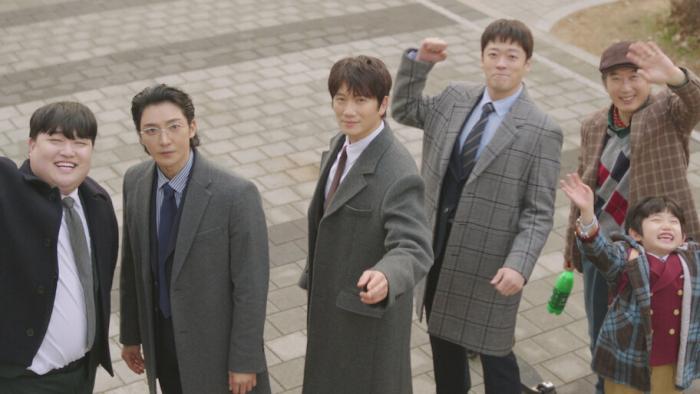 The Apartment Job TV show screenshot: Five Korean men and a child in coats, smiling and waving outdoors on a stone path.