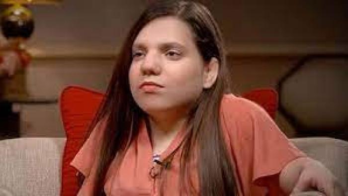 The Curious Case of Natalia Grace TV show screenshot: A closeup shot of a woman with dwarfism is shown as she sits unsmiling on a coach.