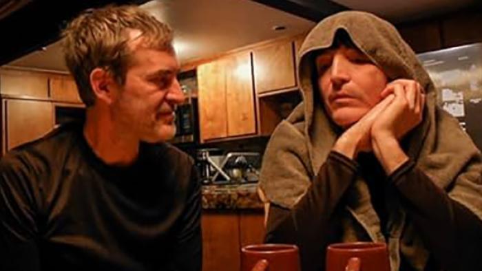 The Creep Tapes screenshot 1: Two men sit at a kitchen table with coffee mugs in front of them. The man on the right has a towel draped over his head