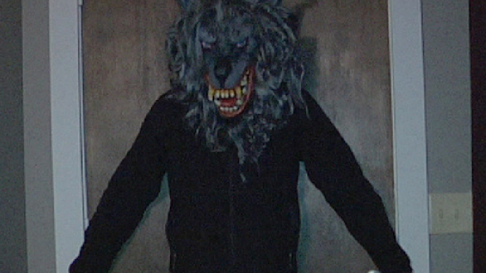 The Creep Tapes screenshot 2: A man in a black sweatshirt and werewolf masks stands with his back and arms against a wooden door