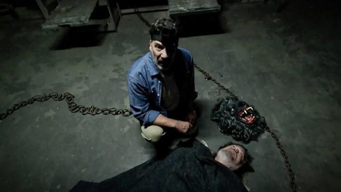 The Creep Tapes screenshot 3: A man kneels on an industrial-looking floor next to an unconscious man flat on his back. Heavy chains lay on the floor 