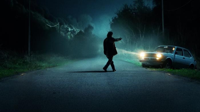 The Monster of Florence TV show screenshot 2: A silhouetted man in the blue light of the night points a gun at a car on a deserted road