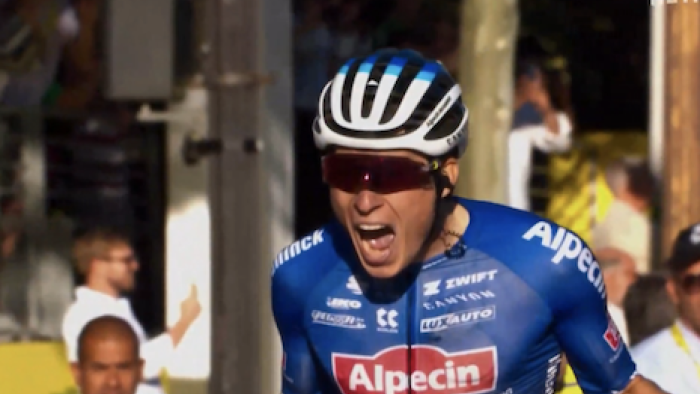 Tour de France: Unchained TV show screenshot 1: A cyclist in blue and red from Alpecin-Deceunick celebrates crossing a stage finish. 