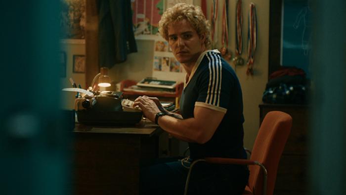 True Haunting TV show screenshot 1: A muscular man with curly blond hair sits at a desk in front of a typewriter, looking over his shoulder