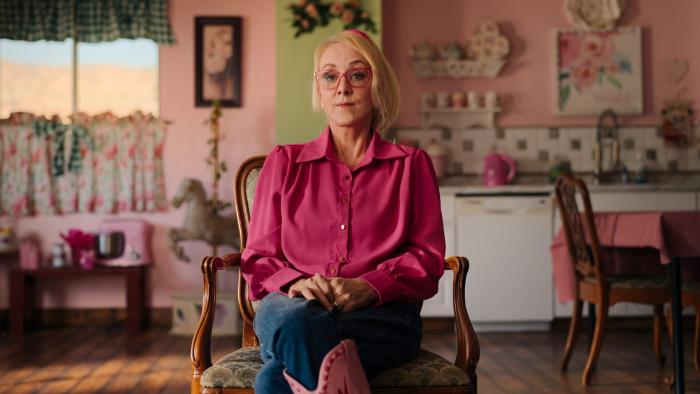 Trust Me: The False Prophet TV show screenshot: Christine Katas sits on a chair in her colorful cottage
