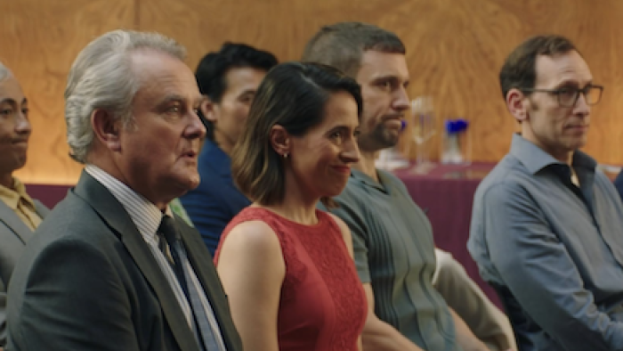 Twenty Twenty Six screenshot 2:People seated attentively in a room with wooden walls and maroon tablecloths.