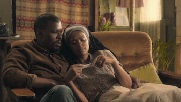 Unseen TV show screenshot 2: Young Max and Zenzi on sofa holding Zenzi's pregnant stomach. 