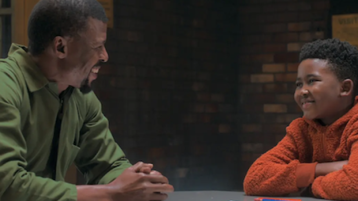 Unseen TV show screenshot 3: Raymond sits at a table talking to Esulu.