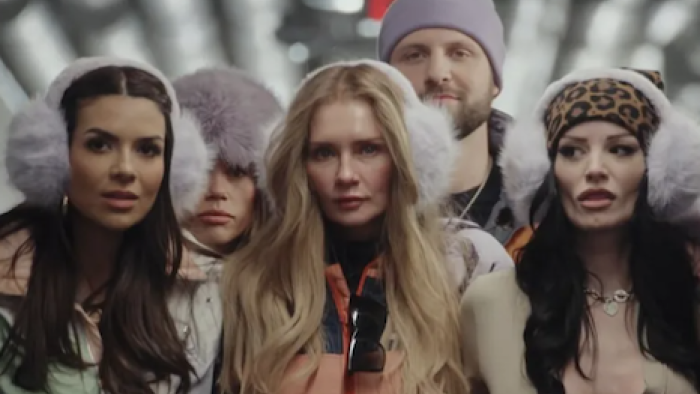 Unwell Winter Games TV show screenshot 2: Anna Delvey Sorokin wear white earmuffs while leading her team through a tunnel.