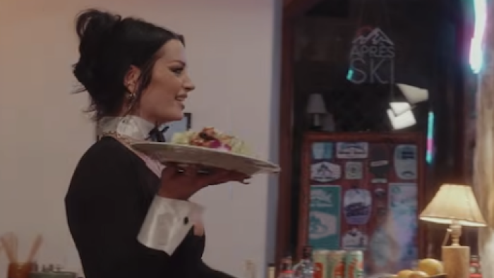 Unwell Winter Games TV show screenshot 3: A member of a losing team holds a plate of food to serve in a black and white uniform.