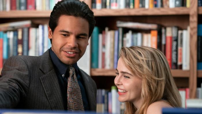 Up Here TV show: Lindsay and Miguel are shown in from the shoulders up in a bookstore, standing close together; they look to be flirting