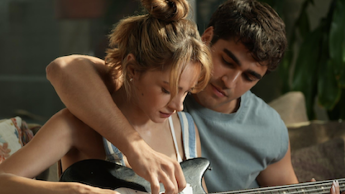 We'll Be Fine TV show screenshot 1: A woman and man playing guitar together on a sofa, focused and relaxed.